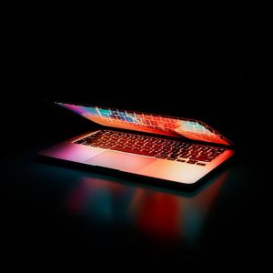 Laptop partially opened, emitting vibrant multicolored lights in dark setting.