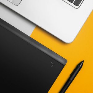 Overhead view of a laptop and graphics tablet on a colorful desk setup.