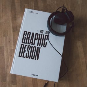 Discover graphic design history with this book and headphones on a wooden floor.